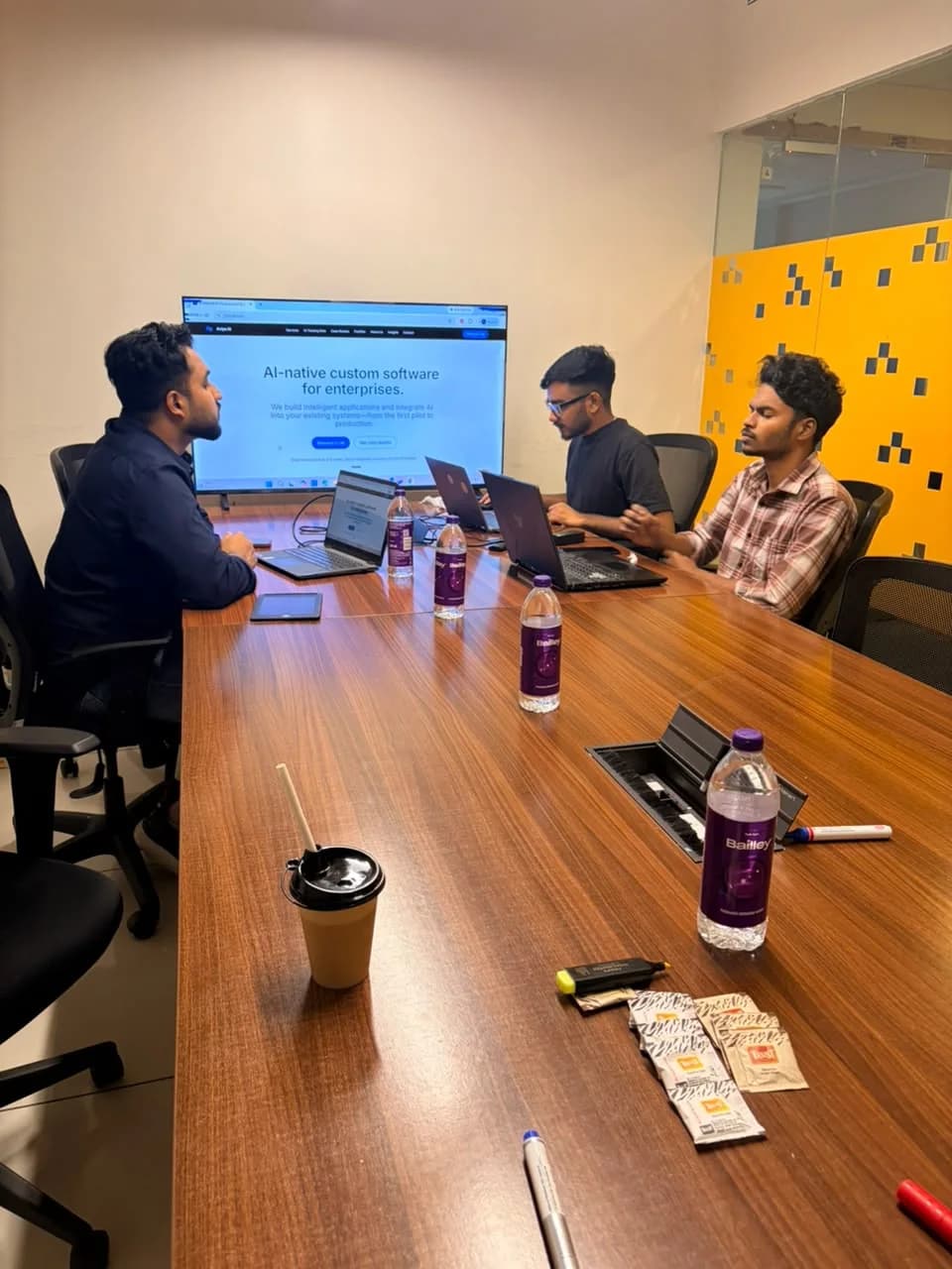 Avlys team members discussing work around a conference table, with the Avlys website on the room display.